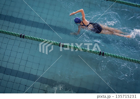 Female swimmer in black swimsuit, blue cap swimming in lap pool with lane dividers, copy space Female swimmer in black swimsuit, blue cap swimming in lap pool with lane dividers, copy space 135715231