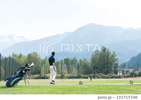 Male golfer practicing swing on tee mat at driving range with golf bag, copy space 135715590