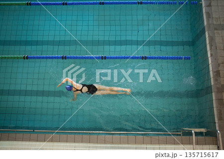 Female swimmer in swimsuit gliding in lap pool, performing front crawl over lane lines and ladder 135715617