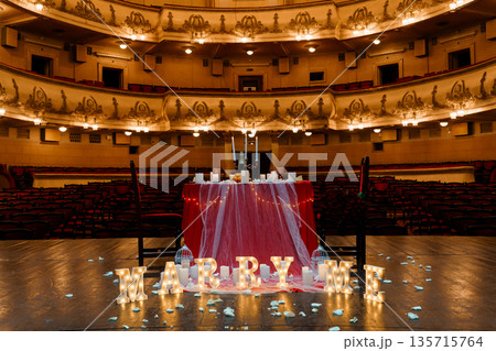 Romantic "MARRY ME" proposal setup with glowing letters and candlelit table in grand theater auditorium Romantic "MARRY ME" proposal setup with glowing letters and candlelit table in grand theater auditorium 135715764