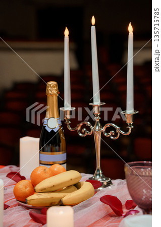 Elegant Valentine's Day Table Setting with Champagne, Candles, Fruit, and Rose Petals in Warm Ambient Lighting 135715785