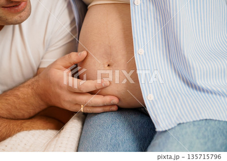 Close-up of a pregnant man's belly being gently touched by a partner in a tender moment, showcasing skin texture and soft lighting Close-up of a pregnant man's belly being gently touched by a partner in a tender moment, showcasing skin texture and soft lighting 135715796