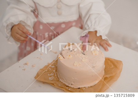 Young girl celebrating first birthday with pink cake and number one candle in soft pastel setting Young girl celebrating first birthday with pink cake and number one candle in soft pastel setting 135715809