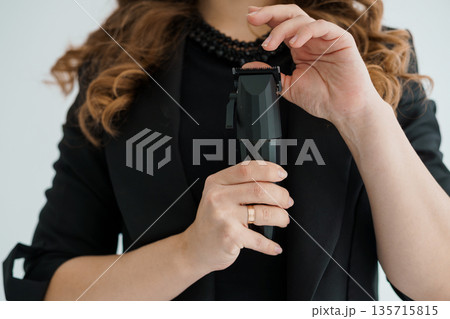 Woman in Black Blazer Using Electric Hair Clipper for Haircut Styling with Long Wavy Hair and Minimalist Background Woman in Black Blazer Using Electric Hair Clipper for Haircut Styling with Long Wavy Hair and Minimalist Background 135715815
