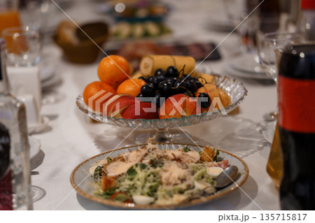 Elegant Table Setting with Fresh Fruit Platter and Caesar Salad in Glass Bowl on White Linen Tablecloth Elegant Table Setting with Fresh Fruit Platter and Caesar Salad in Glass Bowl on White Linen Tablecloth 135715817