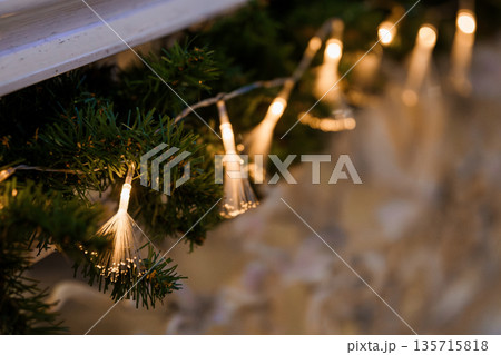 Warm Glowing Fiber Optic Lights Adorning Green Christmas Tree Branches in Cozy Holiday Decor Setting 135715818