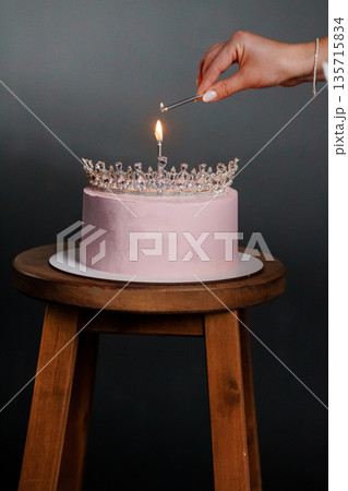 Elegant Pink Birthday Cake Topped with Sparkling Crown Being Lit with Candle Flame Elegant Pink Birthday Cake Topped with Sparkling Crown Being Lit with Candle Flame 135715834