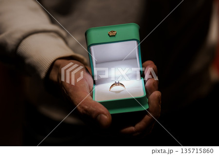 Elegant Engagement Ring in Green Box Held by Hands with Soft Lighting and Warm Background 135715860
