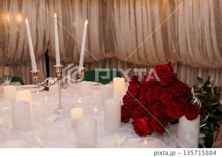 Elegant Wedding Table Setting with Red Roses, Candlelight, and Silver Candelabra on White Tulle Background Elegant Wedding Table Setting with Red Roses, Candlelight, and Silver Candelabra on White Tulle Background 135715884