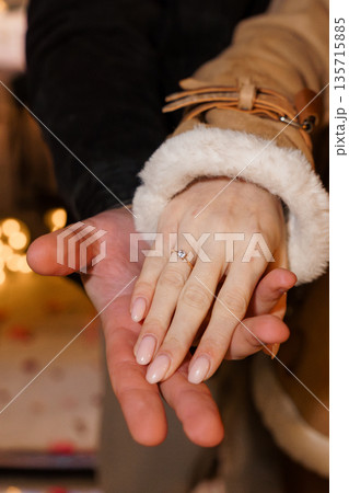 Close-up of an elegant engagement ring on a woman's hand held by a man in a cozy winter setting with warm lighting Close-up of an elegant engagement ring on a woman's hand held by a man in a cozy winter setting with warm lighting 135715885