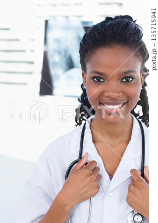 African American female clinician smiling, holding stethoscope and wearing white coat in clinic African American female clinician smiling, holding stethoscope and wearing white coat in clinic 135715941