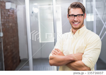 Man standing smiling arms crossed in office wearing glasses and yellow button-up shirt, copy space Man standing smiling arms crossed in office wearing glasses and yellow button-up shirt, copy space 135716037