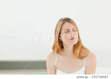 Mid-adult female sitting in bright studio wearing strappy top, pale ledge, eyes closed, copy space Mid-adult female sitting in bright studio wearing strappy top, pale ledge, eyes closed, copy space 135716087