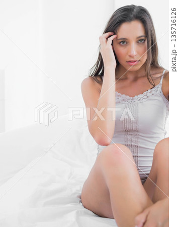 Adult female sitting on white bed touching hair and looking at camera, camisole, copy space Adult female sitting on white bed touching hair and looking at camera, camisole, copy space 135716126