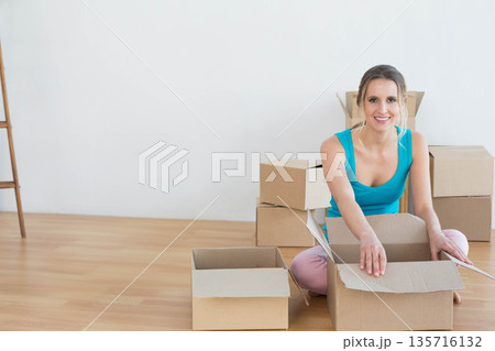 Woman wearing turquoise tank top kneeling handling box flaps in empty room, ladder left, copy space Woman wearing turquoise tank top kneeling handling box flaps in empty room, ladder left, copy space 135716132