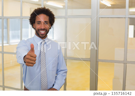 African American man in shirt and tie standing by metal-framed glass partition giving thumbs up 135716142