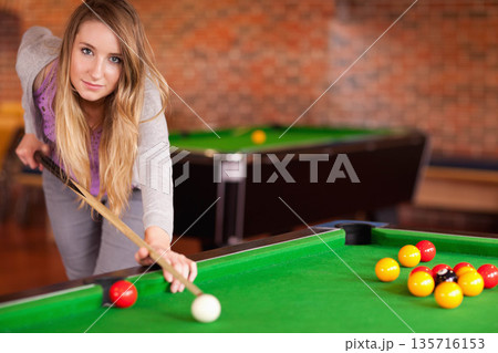 Woman in twenties leaning over pool table in pool hall, aiming cue at white cue ball 135716153