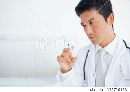 Asian male doctor in clinic white coat stethoscope holding syringe checking needle, copy space Asian male doctor in clinic white coat stethoscope holding syringe checking needle, copy space 135716158