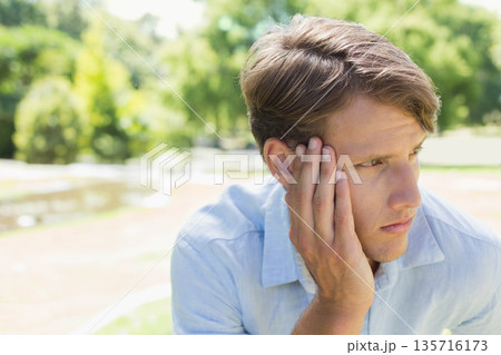 Adult man sitting on park bench wearing light blue collared shirt, resting hand, looking right Adult man sitting on park bench wearing light blue collared shirt, resting hand, looking right 135716173