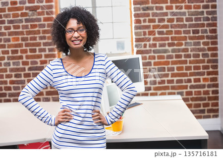African American woman standing hands on hips smiling in office with striped shirt glasses monitor African American woman standing hands on hips smiling in office with striped shirt glasses monitor 135716181