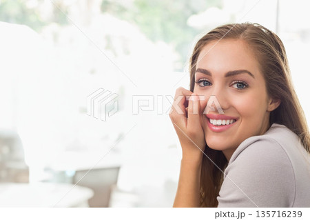 Woman smiling, resting hand against cheek at cafe near blurred tables and windows, copy space 135716239