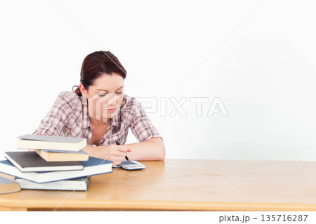 Adult woman working at wooden table in plaid shirt, using calculator and pen, books left Adult woman working at wooden table in plaid shirt, using calculator and pen, books left 135716287