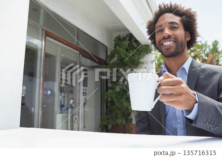 Mid-adult African American in suit jacket, blue shirt, holding white mug at entrance, copy space 135716315