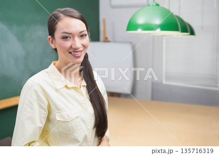 Adult Asian woman wearing yellow shirt standing in classroom, holding marker near chalkboard 135716319