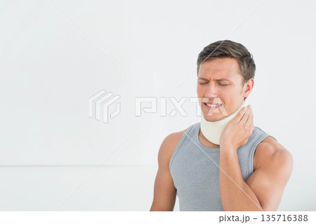 Male standing right by white wall, touching neck, wearing gray tank top and brace, copy space Male standing right by white wall, touching neck, wearing gray tank top and brace, copy space 135716388