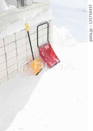 雪が積もった塀に立てかけたママさんダンプと除雪スコップ 135716437