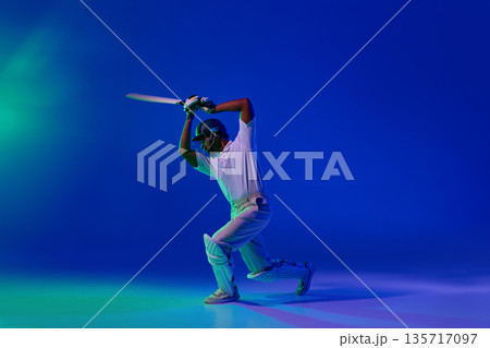 Cricket batsman playing defensive shot in studio with blue light background 135717097