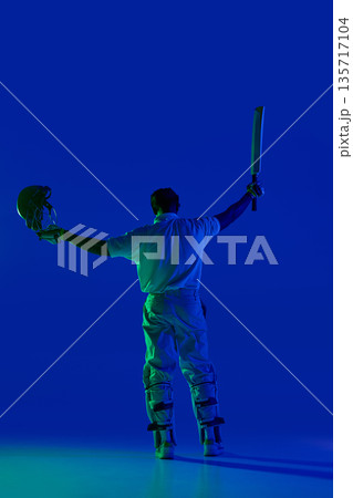 Cricket batsman standing with raised equipment under blue studio light Cricket batsman standing with raised equipment under blue studio light 135717104