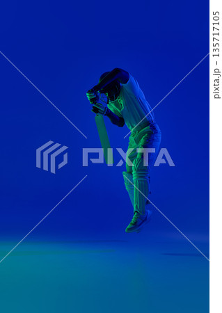 Cricket batsman airborne defensive technique under blue studio light. Cricket batsman airborne defensive technique under blue studio light. 135717105