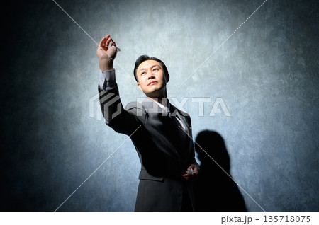 黒い背景でダーツを構えるスーツの男性 135718075