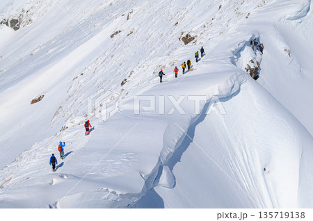 厳冬期の谷川岳・巨大な雪庇の横を通過する登山者 135719138