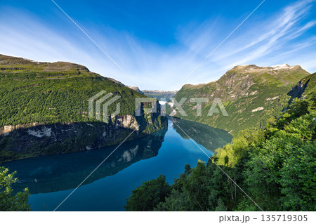 Aerial panoramic view of Geirangerfjord in summer Norway. Scenic panoramic landscape of Geirangerfjord with steep green mountains and calm blue water under clear summer sky in Norway. 135719305