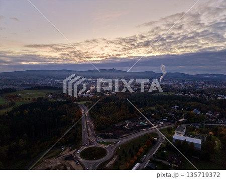 aerial view of evening city junction featuring converging roads and distant industrial emission aerial view of evening city junction featuring converging roads and distant industrial emission 135719372
