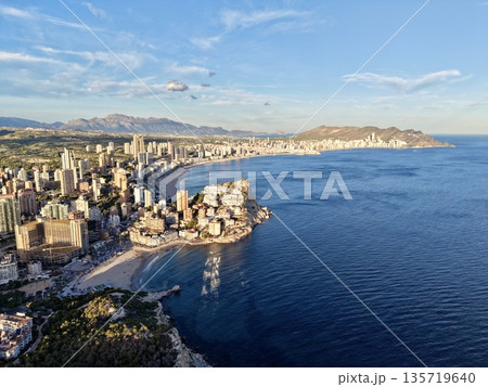 coastal skyline sunrise, beachfront cityscape with morning glow, highrise harbor city illuminated at dawn 135719640