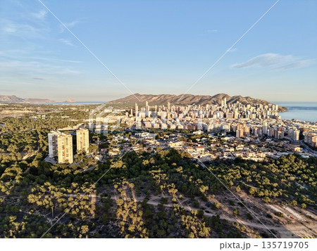 photograph depicting mountain valley flowing into sea with twilight shadows and distant city silhouettes 135719705
