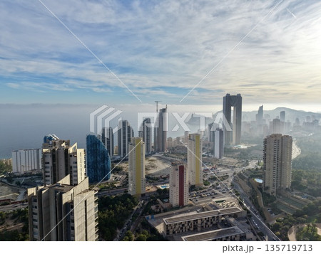 mist surrounds oceanfront cityscape at dawn, serene early morning scene of seafront city and pale mist 135719713