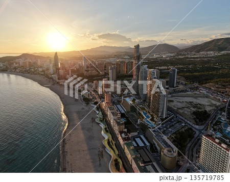 sunrise over harbor with shadows, tower silhouette against vibrant morning sky with textured sand 135719785