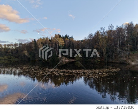 autumnal riverbank with peaceful reflections, silent river clearing bordered by colorful fall foliage 135719830