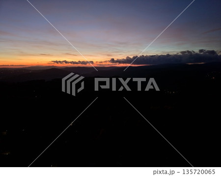 dramatic sunset with cloud band slicing sky, rich colors blending into silhouette ridgeline and calm twilight 135720065
