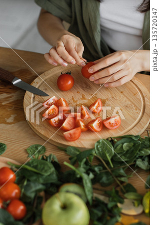 A person is preparing fresh ingredients for a healthy meal, chopping cherry tomatoes on a wooden cutting board with a knife nearby A person is preparing fresh ingredients for a healthy meal, chopping cherry tomatoes on a wooden cutting board with a knife nearby 135720147