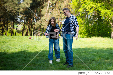 Father And Daughter Practicing Play With Ball On A Rubber String While Spending Time In Summer Park 135720778