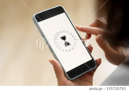 Girl Holds A Smartphone Displaying A Rotating Hourglass To Indicate A Loading Process 135720783