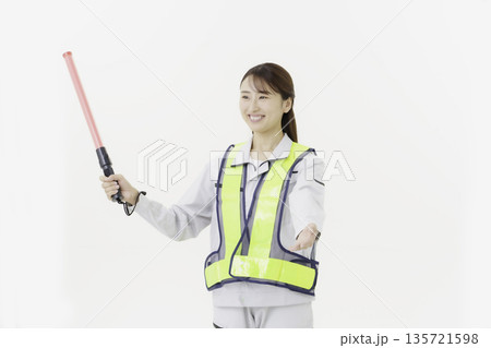 白背景の作業服の安全ベルトをつけて誘導灯を持つ若い日本人女性 135721598
