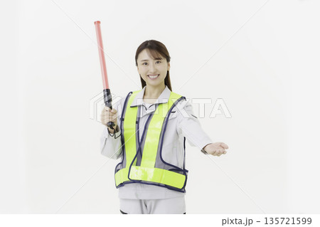 白背景の作業服の安全ベルトをつけて誘導灯を持つ若い日本人女性 135721599