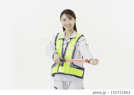 白背景の作業服の安全ベルトをつけて誘導灯を持つ若い日本人女性 白背景の作業服の安全ベルトをつけて誘導灯を持つ若い日本人女性 135721601