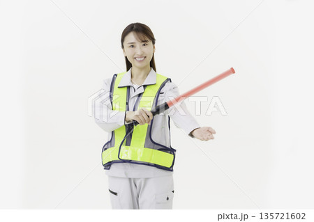 白背景の作業服の安全ベルトをつけて誘導灯を持つ若い日本人女性 白背景の作業服の安全ベルトをつけて誘導灯を持つ若い日本人女性 135721602